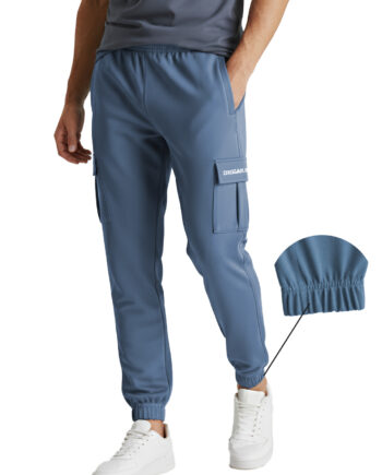 Close-up of a person wearing dusty blue "DEGAN SPORT" cargo track pants, featuring a side flap pocket with white branding and a red woven label on the upper pocket seam.